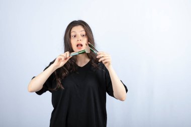 Beyaz arka planda fırçalarla makyaj tozu temizleyen genç ve güzel bir model resmi. Yüksek kalite fotoğraf