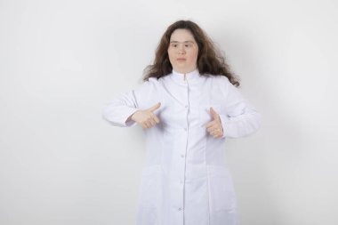 Aşağı sendromlu genç bir kız modelin portresi ayakta ve baş parmağını kaldırıyor. Yüksek kalite fotoğraf