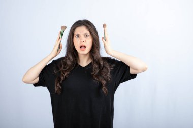 Makyajlı, beyaz arka planda fırçaları olan genç ve güzel bir model. Yüksek kalite fotoğraf