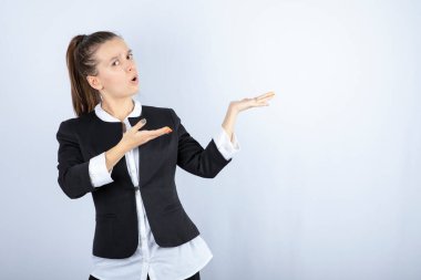 Beyaz arka planda ayakta duran ve açık alan tutan genç bir kadın resmi. Yüksek kalite fotoğraf