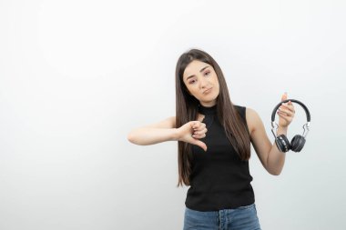 Siyah tişörtlü, kablosuz kulaklıklı, baş parmağını kaldıran sevimli bir kadın. Yüksek kalite fotoğraf