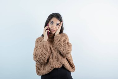 Örgü kıyafetli güzel bir kadının beyaz arka planda cep telefonuyla konuşması. Yüksek kalite fotoğraf