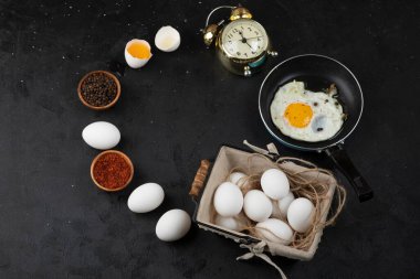 Bir kap sahanda yumurta, baharat ve siyah arka planda çalar saat. Yüksek kalite fotoğraf