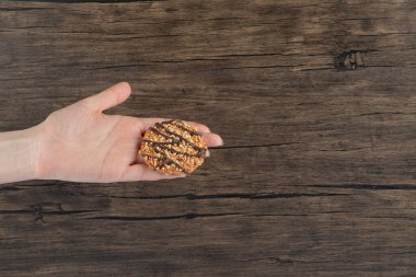 Ahşap zemin üzerinde çikolata şurubu olan yulaflı kurabiye tutan kadın eli. Yüksek kalite fotoğraf