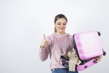 Genç, güzel bir model bavulu açıyor ve baş parmağını kaldırıyor. Yüksek kalite fotoğraf