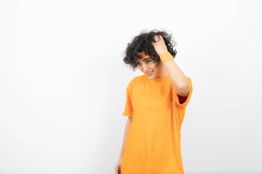 Turuncu tişörtlü kadın beyaz arka planda poz veriyor.