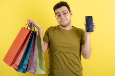 Elinde boş cep telefonu ve alışveriş torbaları olan yakışıklı bir adamın fotoğrafı. Yüksek kalite fotoğraf