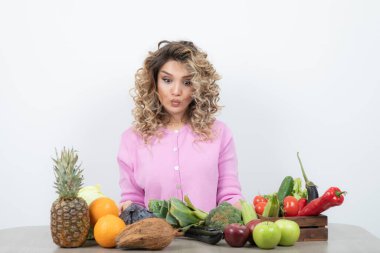 Masada çeşitli meyve ve sebzelerle poz veren güzel bir kadın.