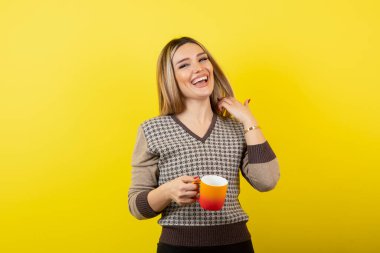 Sarı arka planda kahve fincanı olan genç bir kadın.