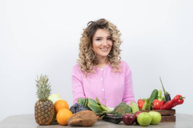 Masada çeşitli meyve ve sebzelerle poz veren güzel bir kadın.