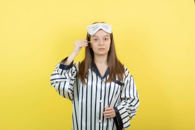 Sarı duvara maskara süren pijamalı genç bir kadın. Yüksek kalite fotoğraf