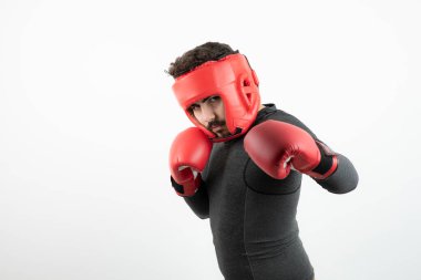 Beyaz duvarın üzerinde boks kaskı ve eldivenleri olan genç bir adamın portresi. Yüksek kalite fotoğraf