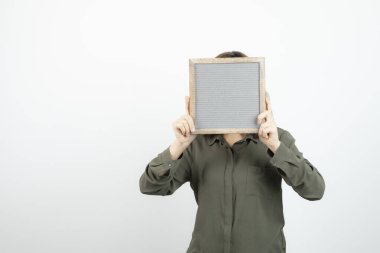 Beyazın üzerinde boş çerçevenin arkasına saklanan sevimli genç bir kadın resmi. Yüksek kalite fotoğraf