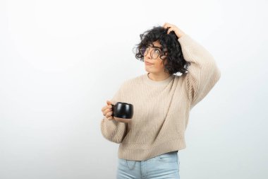 Beyazın üzerinde duran bir fincan çayla kıvırcık saçlı genç kadın. Yüksek kalite fotoğraf