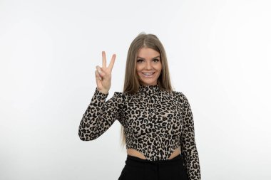 Güzel kadın gülümsüyor ve beyaz duvara karşı zafer işareti gösteriyor. Yüksek kalite fotoğraf