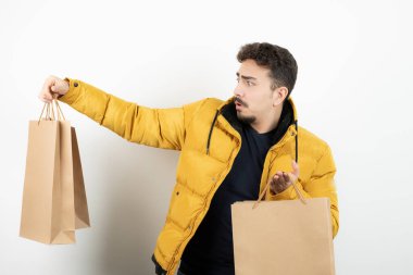 Beyaz bir duvarın üzerinde kağıt torbaları tutan genç bir adam. Yüksek kalite fotoğraf