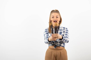 Beyaz bir duvarın üzerinde duran ve elinde boya fırçaları tutan muhteşem bir kadın sanatçı. Yüksek kalite fotoğraf