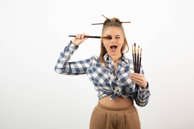 Beyaz bir duvarın üzerinde fırça tutan ve poz veren genç bir sanatçının portresi. Yüksek kalite fotoğraf