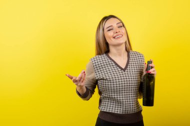 Sarı arka planda şarap şişesiyle poz veren güzel bir kadın.