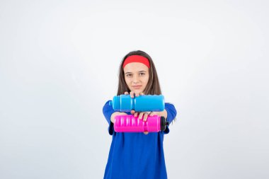 Mavi tişörtlü, kırmızı bileklikli ve beyaz arka planda plastik şişelerle poz veren kız.