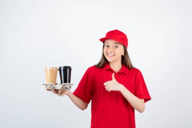 Kırmızı tişörtlü ve şapkalı kız tek kullanımlık bardaklarla poz veriyor.