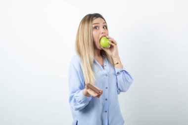 Taze yeşil bir elmayı ısırmaya çalışan ve elinde çikolata tutan bir kadın. Yüksek kalite fotoğraf