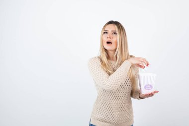 Beyaz duvara karşı duran ve elinde patlamış mısır taşıyan genç bir kadın resmi. Yüksek kalite fotoğraf