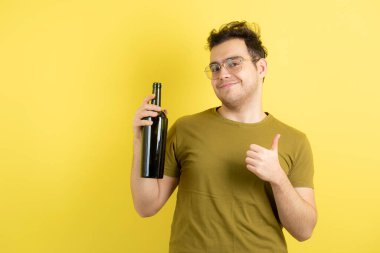 Genç mankenin elinde bir şişe beyaz şarap tutarken ve baş parmağını kaldırırken fotoğrafı. Yüksek kalite fotoğraf