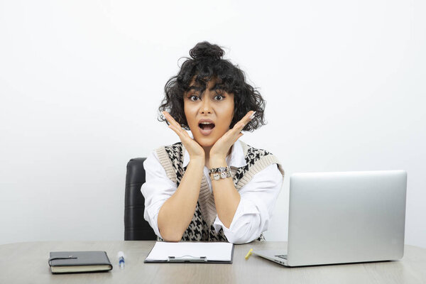 Молодая деловая женщина сидит за столом с ноутбуком и смотрит в камеру. Высокое качество фото