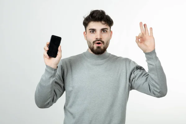 Portret Atrakcyjnego Faceta Trzymającego Smartfon Robiącego Znak Wysokiej Jakości Zdjęcie — Zdjęcie stockowe