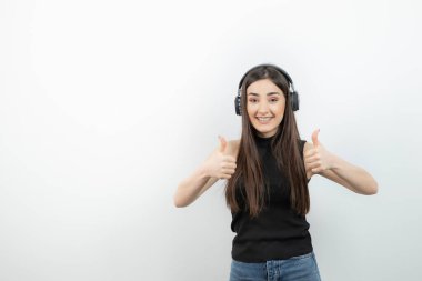 Siyah tişörtlü, kablosuz kulaklıklı, baş parmağını kaldıran sevimli bir kadın. Yüksek kalite fotoğraf