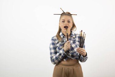 Beyaz bir duvarın üzerinde boya fırçaları tutan ve poz veren zevkli bir sanatçı. Yüksek kalite fotoğraf