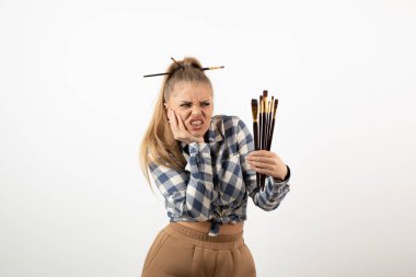 Beyaz bir duvarın üzerinde fırça tutan ve poz veren genç bir sanatçının portresi. Yüksek kalite fotoğraf