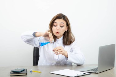 Bayan laboratuvar araştırmacısı masada oturuyor ve elinde mavi sıvıyla tıbbi cam şişe tutuyor. Yüksek kalite fotoğraf