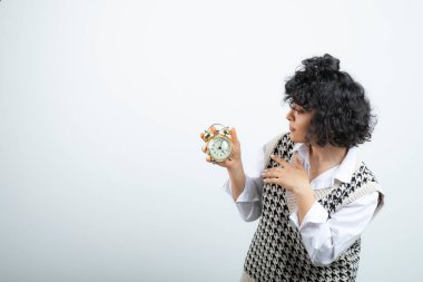 Saatin alarmına bakan kıvırcık bir genç kadın resmi. Yüksek kalite fotoğraf