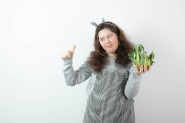 Kıvırcık saçlı, sağlıklı karnabaharı olan ve baş parmağını gösteren güzel bir kızın fotoğrafı. Yüksek kalite fotoğraf