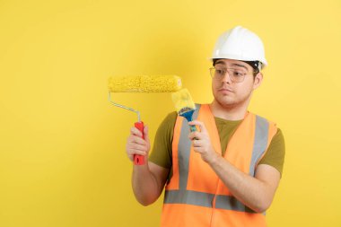 Şapkalı genç inşaat işçisi elinde boya rulosu ve fırçasıyla. Yüksek kalite fotoğraf