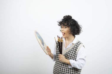 Fırçalar ve palet boyasıyla ayakta duran genç bir kadın sanatçı. Yüksek kalite fotoğraf