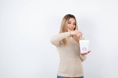 Beyaz duvara karşı duran ve elinde patlamış mısır taşıyan genç bir kadın resmi. Yüksek kalite fotoğraf