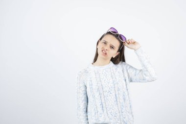 Beyaz arka planda güneş gözlüğü takan süveter giyen kız