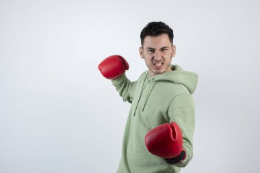 Kendine güvenen genç sporcu beyaz duvara karşı boks eldivenleriyle yumruk atıyor. Yüksek kalite fotoğraf