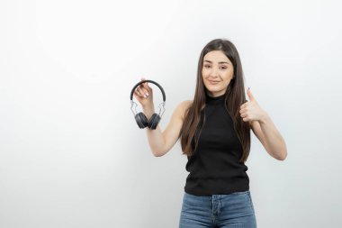 Kulaklık tutan genç bir kadının portresi baş parmaklarını gösteriyor. Yüksek kalite fotoğraf