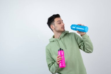 Kapüşonlu genç sakallı adamın renkli su şişelerini tutuşu. Yüksek kalite fotoğraf