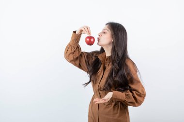 Beyaz duvarda kırmızı elma yiyen esmer bir kız resmi. Yüksek kalite fotoğraf