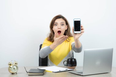 Masada oturan ve elinde cep telefonu tutan kadın ofis çalışanının fotoğrafı. Yüksek kalite fotoğraf