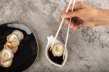 Erkek eli soya soslu suşi rulosunu taş bir masanın üzerine koyuyor. Yüksek kalite fotoğraf