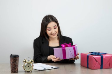 İş yerinde elinde hediyelerle oturan iş kadınının portresi.