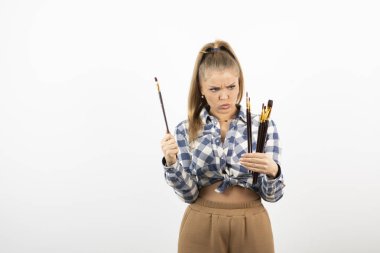 Beyaz bir duvarın üzerinde fırça tutan ve poz veren genç bir sanatçının portresi. Yüksek kalite fotoğraf