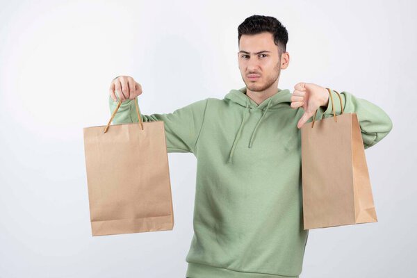 Handsome man in green hoodie with paper bags showing thumb down. High quality photo
