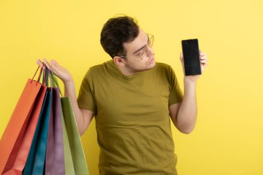 Elinde boş cep telefonu ve alışveriş torbaları olan yakışıklı bir adamın fotoğrafı. Yüksek kalite fotoğraf